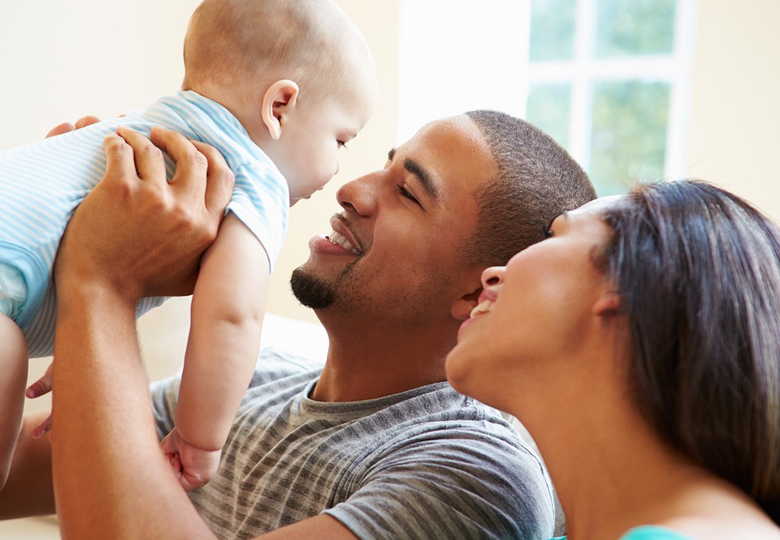 Young Family Playing With Happy Baby Son At Home